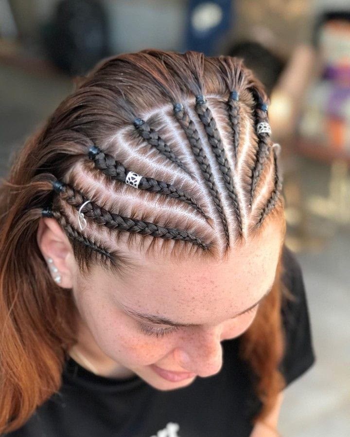 Fan-shaped stitch cornrows with silver cuffs on copper-toned hair, seen from above.