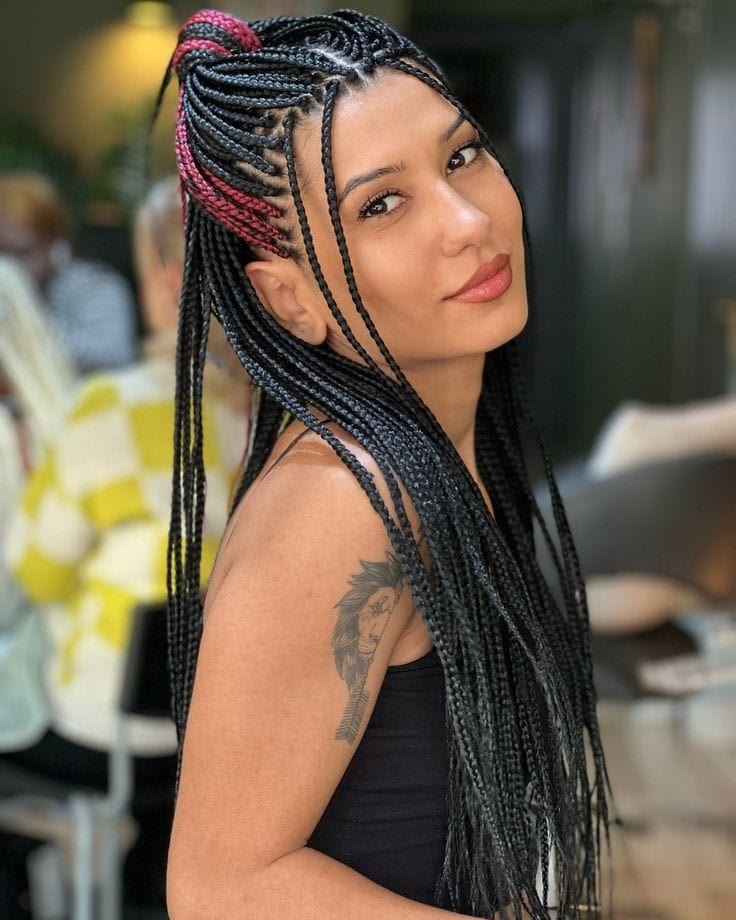 Long knotless braids in black with a soft pink accent, gathered in a half-up style, seen inside the salon.